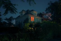 a house is lit up at night with red lights on the windows and shutters