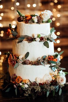 a three tiered cake with flowers and greenery on the top is sitting on a table