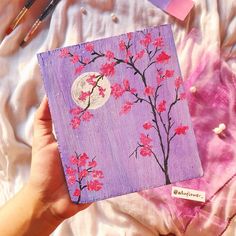 someone is holding up a purple notebook with pink flowers and a full moon in the background