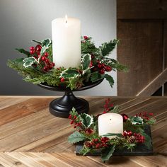 two candles are sitting on a table with holly and berries