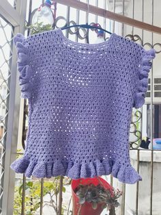 a purple crocheted top is hanging on a metal rack next to a red fire hydrant