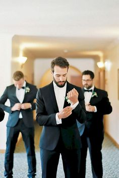 a man in a tuxedo is adjusting his tie while another man stands behind him