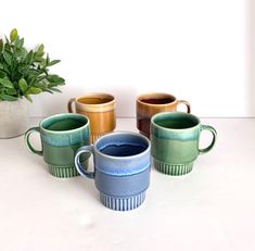 four coffee mugs sitting next to a potted plant on a white countertop