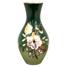 a green vase with white flowers painted on the side and gold trim around the bottom