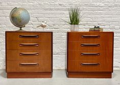 two nightstands with drawers and a globe on top, against a white brick wall