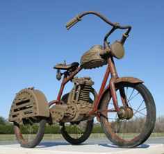 an old rusty motorcycle sitting in the middle of a grassy field with blue skies behind it