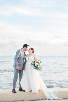 a bride and groom standing on the beach