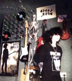 a man standing in front of a wall with various items on it and a guitar