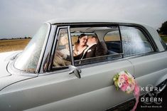 a bride and groom kissing in the back seat of an old car on their wedding day