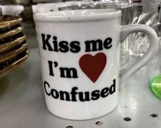 a coffee cup with the words kiss me i'm confused on it next to some glasses