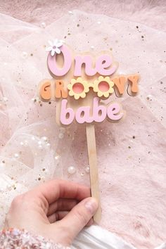 a hand holding a wooden sign that says one groovy babe in pink and yellow