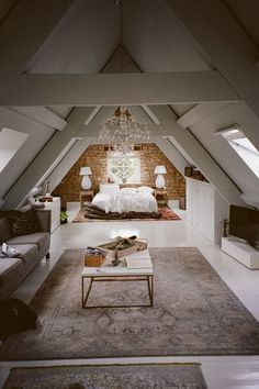 an attic bedroom with white walls and exposed ceilings, carpeted flooring, two couches, coffee table, chandelier