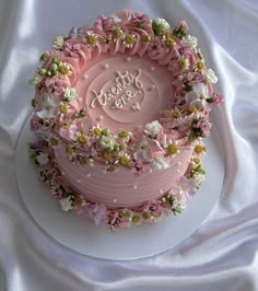 there is a pink cake with flowers on the top that says happy birthday and it's frosting