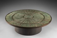 a round table with an intricate design on it's top, sitting in front of a gray background