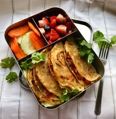 a lunch box with fruit, vegetables and tortilla wraps in it next to a fork