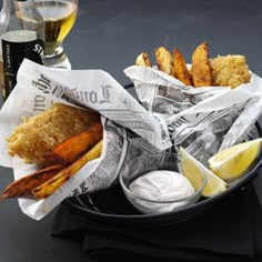 fish and chips with lemon wedges on a black plate next to a glass of beer