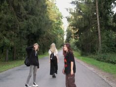 three young women standing on the side of a road with trees in the back ground