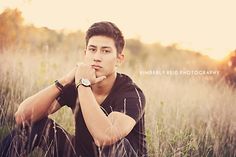 a young man sitting in the grass with his hands on his chin and looking at the camera