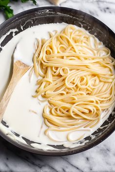 a pan filled with pasta and sauce on top of a marble countertop next to a wooden spoon