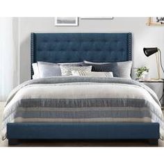 a bed with blue upholstered headboard in a white and gray bedroom setting