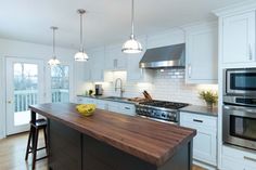 a kitchen with white cabinets and wood counter tops, an island in the middle is surrounded by stools