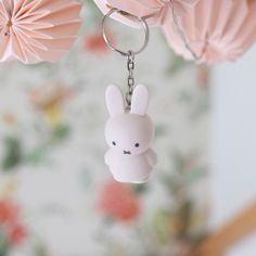 a keychain with a bunny on it hanging from the ceiling in front of flowers