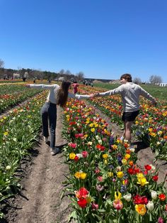 two girls are walking through a field full of tulips and other colorful flowers