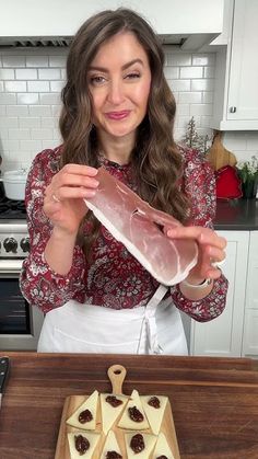 a woman holding up a piece of meat on top of a wooden cutting board next to some crackers