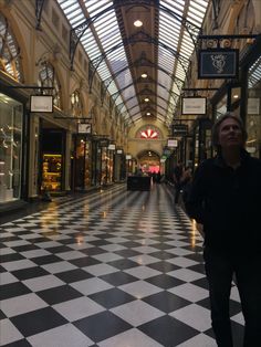 a man is standing in the middle of an empty shopping mall with black and white checkered floors