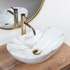 a white marble sink sitting on top of a wooden counter next to a round mirror