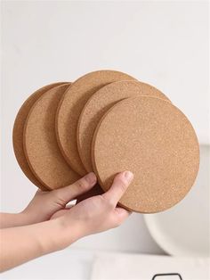 a person holding four cork coasters in their hand