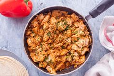 a skillet filled with chicken and vegetables next to tortilla shells on a blue surface