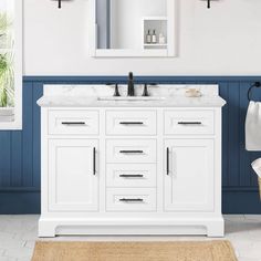 a white bathroom vanity with two mirrors and blue paint on the walls, along with an area rug