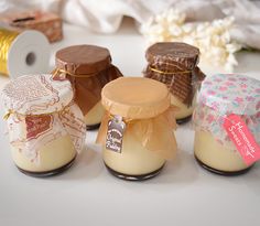 small jars filled with different types of desserts on a white tablecloth next to some spools of thread