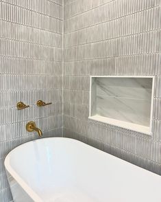 a white bath tub sitting in a bathroom next to a mirror and tiled wall behind it