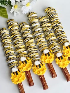 several yellow and black candy sticks are lined up on a white surface with flowers in the background