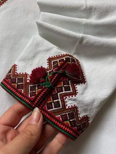 someone is stitching something on top of a white shirt with red and green trim