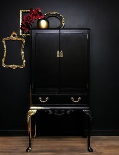 a black cabinet with gold trim and flowers on top, against a black wall behind it