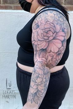 a woman with a flower tattoo on her arm and arms is standing in front of a brick wall