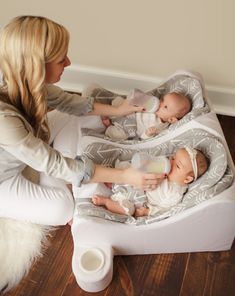 a woman sitting on the floor with two babies in her lap and one holding a bottle