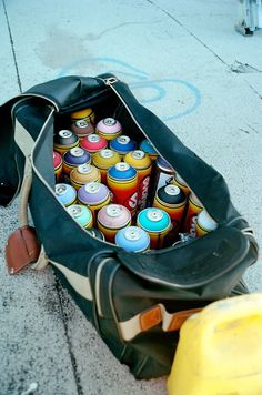 a duffel bag full of soda cans sitting on the sidewalk next to a yellow fire hydrant