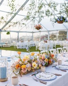 a table set up with flowers and place settings for an outdoor wedding reception in a tent