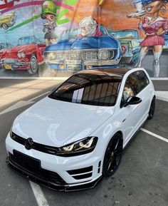 a white volkswagen car parked in front of a wall with colorful paintings on it's side