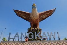 a large bird statue sitting on top of a cement wall next to the words langkaw