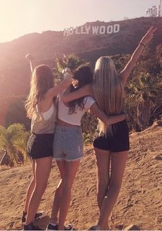 three young women standing on top of a sandy hill with their arms in the air