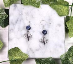 two pairs of earrings on top of a marble slab with green leaves around them and one pair is dangling from the ear