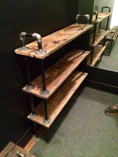 a wooden shelf with metal pipes on it in front of a black wall and green carpet