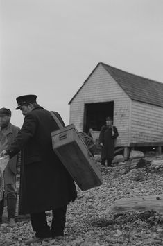 an old photo of two men walking on the beach with suitcases in their hands