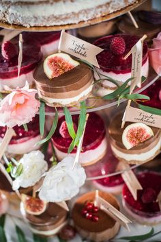 there are many desserts on the table and one is decorated with flowers, leaves and berries