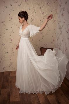 a woman in a white dress standing on a wooden floor next to a wall with flowers